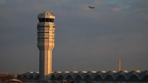 برج المراقبة في مطار ريغان الوطني مع طائرة تحلق في السماء، خلفه نصب واشنطن، في سياق تحقيق حول هبوط غير مكتمل لرحلات تجارية.