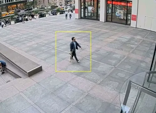 شخص يرتدي نظارات شمسية ويحمل بندقية هجومية، يسير نحو مدخل مبنى مكاتب في نيويورك، حيث وقعت حادثة إطلاق نار.