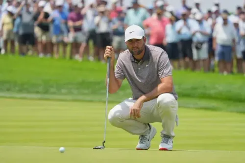 لاعب الجولف سكوتي شيفلر يستعد لضرب الكرة على العشب الأخضر في ملعب أوكمونت، حيث يتواجد جمهور كبير خلفه.