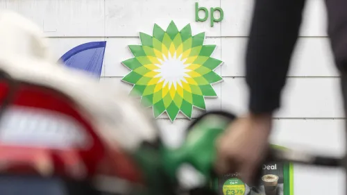 شعار شركة BP على جدار محطة الوقود، مع شخص يحمل مضخة وقود، يعكس خطط الشركة لخفض التكاليف وتقليل عدد الموظفين.