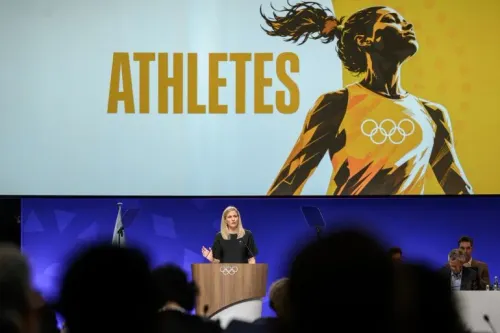 خلال اجتماع اللجنة الأولمبية الدولية، تظهر رئيسة اللجنة Kirsty Coventry وهي تتحدث عن دعم الرياضيين، مع خلفية تحمل كلمة "ATHLETES".