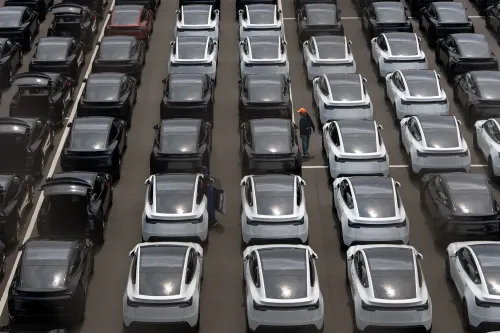 صفوف من سيارات تسلا الجديدة في موقف سيارات، مع وجود شخص يعمل بين السيارات، تعكس تراجع المبيعات والأرباح.