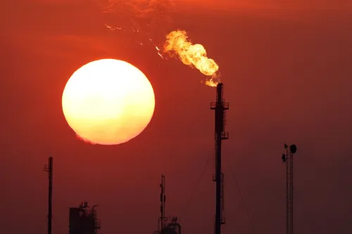 شمس تغرب خلف مداخن صناعية تطلق لهبًا، مما يرمز لزيادة إنتاج النفط في أوبك+ وسط مخاوف من تعطل الإمدادات.