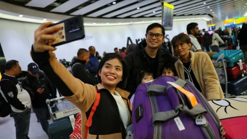 مسافرون مبتسمون يلتقطون سيلفي في مطار هيثرو بلندن، مع حقائبهم في الخلفية، بعد استئناف الرحلات الجوية بعد انقطاع التيار الكهربائي.