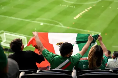 مشجعون يرتدون قمصان المنتخب المكسيكي يحملون علم المكسيك في ملعب سوفي، مع أجواء حماسية قبل مباراة كرة القدم.