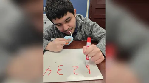 شاب يجلس أمام لوح أبيض، يحتسي مشروبًا من علبة صغيرة، ويستخدم قلمًا لتدوين أرقام حمراء، مع التركيز على الكتابة.