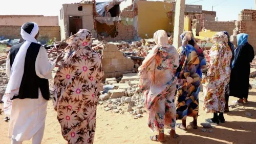 نساء سودانيات يرتدين ملابس تقليدية يقفن أمام منازل مدمرة في كردفان، تعبيراً عن أزمة النزوح والتدمير الناتجة عن الحرب والفيضانات.