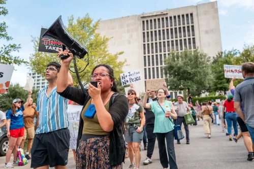 تجمع حشود من المتظاهرين في أوستن، تكساس، مع لافتات ضد استيلاء ترامب على السلطة، حيث يتحدث أحدهم عبر مكبر صوت.