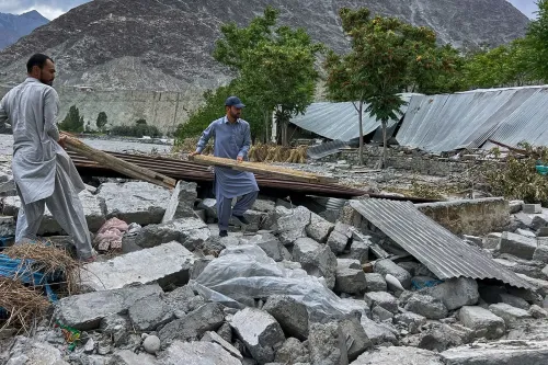 شخصان يجمعان حطام المنازل المدمرة بفعل الفيضانات في باكستان، مع خلفية جبال وقمم صخرية، مما يعكس آثار تغير المناخ.