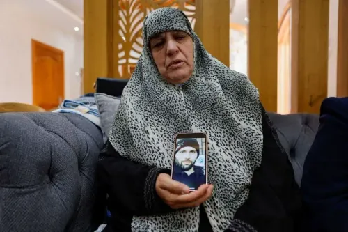 امرأة مسنّة ترتدي حجابًا، تجلس على أريكة وتظهر صورة لابنها الراحل، تعبيرها يعكس الحزن بعد مقتل الفلسطيني خميس عياد في هجوم للمستوطنين.