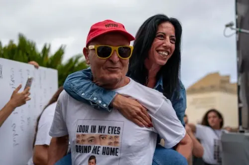 احتفال شخصين في تجمع عام، حيث يحمل رجل مسن امرأة على ظهره، ويظهر على قميصه عبارة "انظر في عينيّ، أعدني إلى المنزل"، تعبيرًا عن الفرح بعد إعلان وقف إطلاق النار.