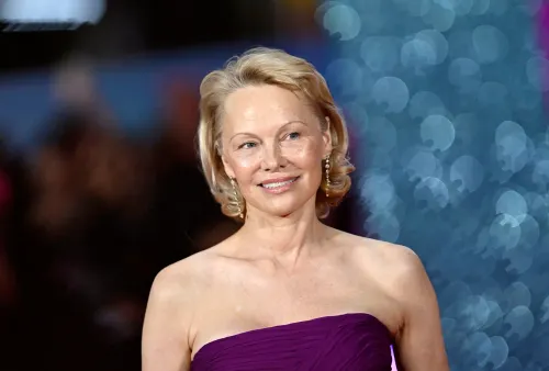 باميلا أندرسون تتألق بفستان أرجواني في حدث ترويجي، مع خلفية لامعة تعكس عودتها القوية إلى عالم الترفيه.