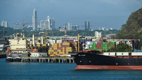 ميناء مزدحم في منطقة قناة بنما، يظهر سفينة شحن كبيرة محملة بالحاويات، مع خلفية لمدينة حديثة وأبراج.