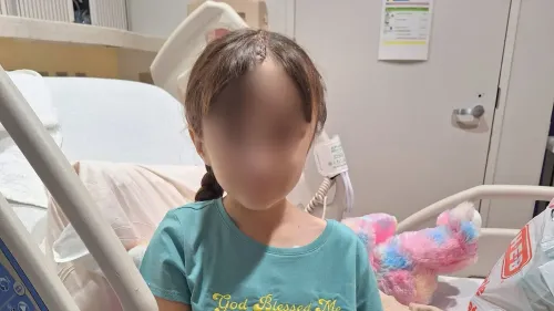 طفلة تبلغ من العمر 10 سنوات تجلس على سرير مستشفى، تعاني من آثار جراحة لإزالة ورم في المخ، محاطة بألعابها.