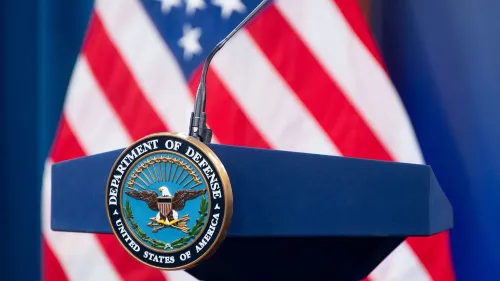 شعار وزارة الدفاع الأمريكية على منصة الإحاطة الإعلامية، مع العلم الأمريكي في الخلفية، يعكس التغييرات في وسائل الإعلام بالبنتاغون.
