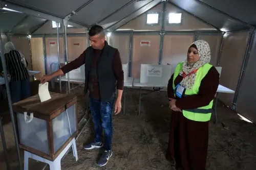 ناخب فلسطيني يدلي بصوته في مركز اقتراع بدير البلح، بينما تراقبه موظفة انتخابية، في أول انتخابات بلدية منذ 20 عاماً.