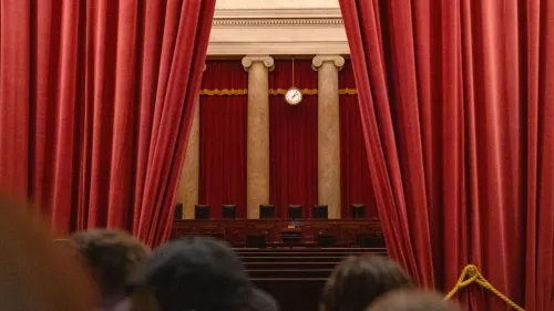 صورة لقاعة المحكمة العليا الأمريكية، تظهر ستائر حمراء وأعمدة، مما يعكس الأجواء الرسمية والتاريخية للمؤسسة القانونية في سياق التحديات القانونية الحالية.