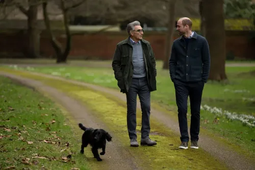 يوجين ليفي والأمير ويليام يتجولان في حديقة قلعة وندسور، يتبادلان الحديث مع كلب أسود صغير بجانبهما، في لحظة غير رسمية ومريحة.