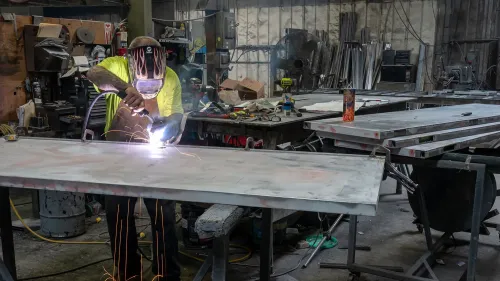 عامل يقوم باللحام في ورشة عمل، حيث تظهر الشرارات أثناء العمل، مما يعكس نشاط التوظيف في قطاع السلع.