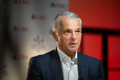 رئيس بنك يو بي إس يتحدث في مؤتمر، مع خلفية تحمل شعار البنك، حيث يتناول أداء البنك المالي والتحديات الاقتصادية.