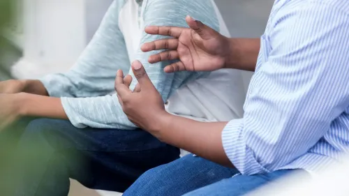 محادثة بين شخصين، أحدهما يستخدم يده للتعبير عن مشاعر حول موضوع حساس، مما يعكس أهمية التحدث عن سن البلوغ.