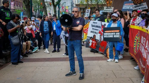 تجمع حاشد في فيلادلفيا لدعم المهاجرين، حيث يتحدث رجل عبر مكبر صوت وسط لافتات تعبر عن الترحيب بالمهاجرين.