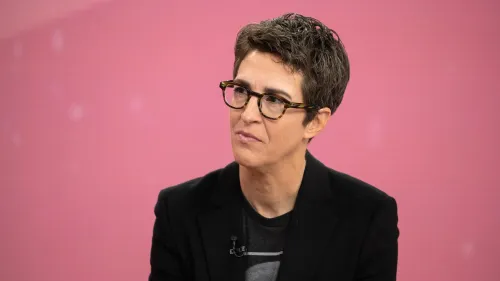 راشيل مادو تتحدث بجدية، مرتدية نظارات، في خلفية وردية، تعبر عن قلقها بشأن إلغاء برامج MSNBC وتأثيره على الموظفين.