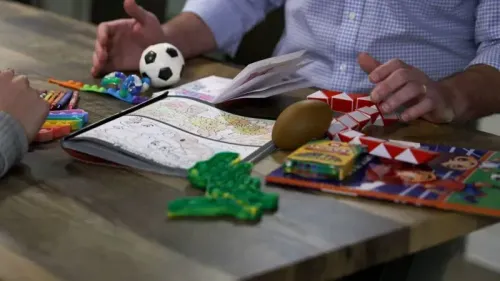 أدوات تلوين وألعاب على طاولة، مع شخصين يتفاعلان أثناء شرح عملية محكمة الهجرة للأطفال المهاجرين.