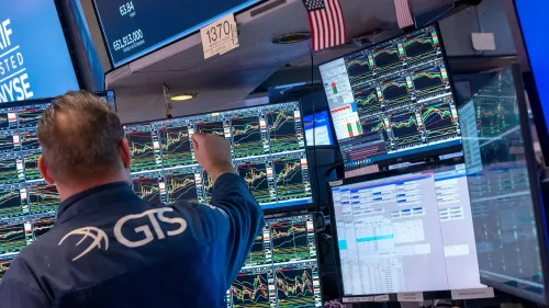 متداول في وول ستريت يتفاعل مع شاشات متعددة تعرض بيانات السوق، مع مؤشرات على تراجع الأسهم بسبب الرسوم الجمركية.
