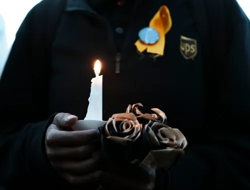 شخص يحمل شمعة مضاءة وزهورًا سوداء، يعبر عن الحزن بعد حادث تحطم طائرة UPS في لويزفيل، مما أدى إلى خسائر بشرية كبيرة.