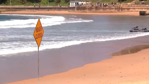 شاطئ مغلق في سيدني بعد هجوم سمكة قرش، مع لافتة تحذر الزوار من دخول المياه، وأمواج تتلاطم على الرمال.