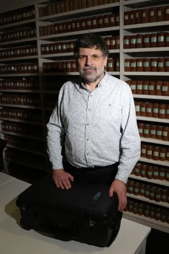 أستاذ يقف أمام مجموعة من الحاويات في مختبر، يحمل حقيبة، في سياق إعادة رفات رجل من السكان الأصليين إلى تسمانيا.