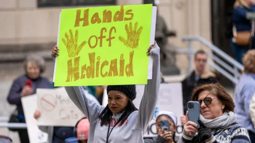 امرأة تحمل لافتة مكتوب عليها "أيدي بعيدة عن Medicaid"، بينما يتجمع المتظاهرون في احتجاج ضد تخفيضات برنامج Medicaid.