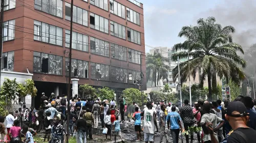 سكان غوما يتجمعون في الشارع أمام مبنى متضرر، مع تصاعد الدخان في الخلفية، خلال تصاعد العنف إثر سيطرة المتمردين على المدينة.