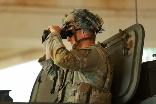 جندي أمريكي يرتدي زيًا عسكريًا، يستخدم مناظير لمراقبة منطقة معينة، في سياق التوترات حول تجارة المخدرات على الحدود المكسيكية.