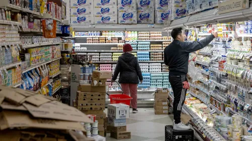 متسوقون في متجر بقالة، أحدهم يرتب المنتجات على الرفوف بينما الآخر يحمل سلة تسوق، وسط أجواء تشير إلى تراجع الإنفاق الاستهلاكي.