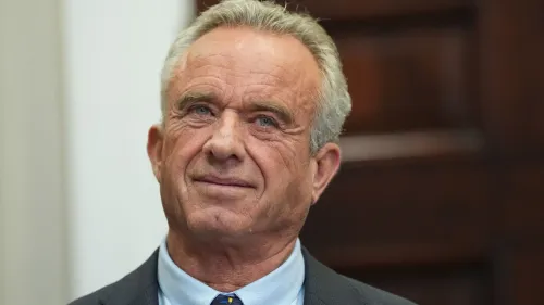 صورة لروبرت ف. كينيدي جونيور، وزير الصحة، يظهر فيها وهو يبتسم بينما يواجه الكاميرا، مع خلفية غير واضحة.