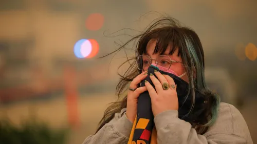 امرأة ترتدي كمامة وتغطي وجهها بيدها، تعبيرها يدل على القلق بسبب الهواء الملوث الناتج عن حرائق الغابات في لوس أنجلوس.
