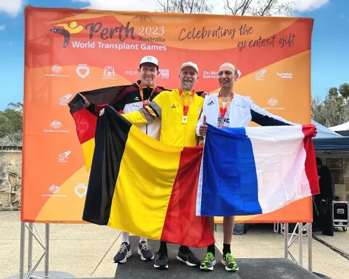 ثلاثة رياضيين يحملون أعلام بلدانهم (بلجيكا، ألمانيا، فرنسا) في دورة الألعاب العالمية لزراعة الأعضاء 2023 في بيرث، أستراليا، مع ميدالياتهم.