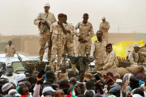 جنود من قوات الدعم السريع شبه العسكرية يقفون على مركبة عسكرية وسط حشد من المدنيين، مع وجود أسلحة ثقيلة في الخلفية، في سياق الصراع في شمال كردفان.