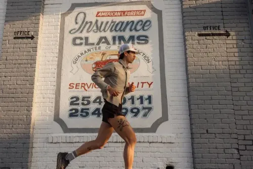 عداء يرتدي ملابس رياضية خفيفة يركض بجانب جدار يحمل شعار خدمات التأمين، مع التركيز على أسلوب الحياة والجري.