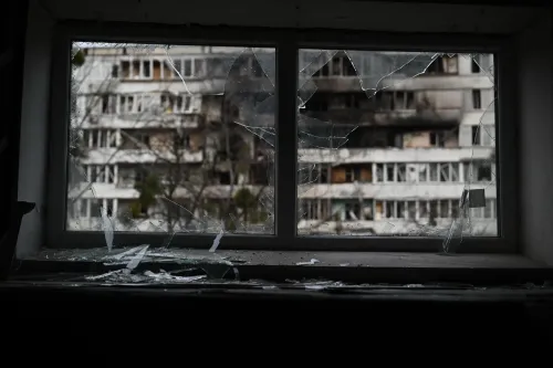 شباك مكسور يطل على مباني مدمرة في أوكرانيا، يعكس آثار الحرب والدمار الذي خلفته الضربات الجوية.