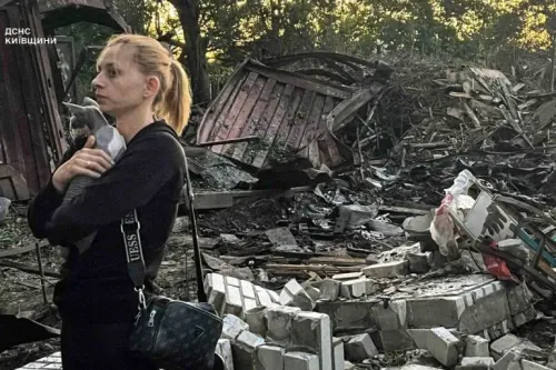 امرأة تحمل قطة في حضنها تقف أمام أنقاض مدمرة، تعكس آثار الهجمات الروسية على أوكرانيا وتأثيرها على المدنيين.