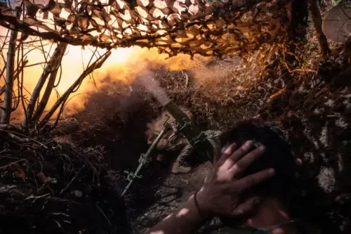 جنود أوكرانيون في خندق أثناء إطلاق قذيفة مدفعية، مع تصاعد الدخان والانفجارات في الخلفية، في سياق الصراع المستمر.