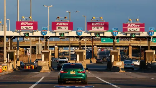 ممر رسوم مرور مع لافتات "EZPass ONLY" تشير إلى ضرورة استخدام بطاقة EZPass للدفع، مع حركة مرور نشطة في الخلفية.