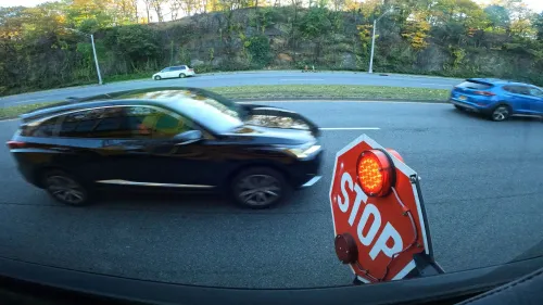 سيارة سوداء تتجاوز علامة توقف حمراء مضاءة على جانب حافلة مدرسية، مما يبرز مخاطر المرور حول محطات الحافلات.