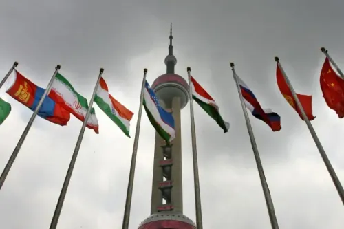 أعلام الدول الأعضاء في منظمة شنغهاي للتعاون ترفرف أمام برج في مدينة صينية، مع سماء غائمة، تعكس أهمية القمة المقبلة.