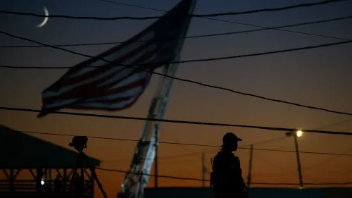 ظل عميل من جهاز الخدمة السرية الأمريكي أمام علم الولايات المتحدة، مع مشهد غروب الشمس في الخلفية، خلال تجمع في بنسلفانيا.