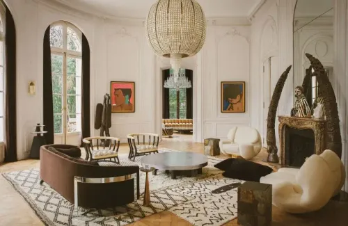 غرفة معيشة أنيقة في منزل ليني كرافيتز في باريس، تتميز بديكورات فنية وأثاث عصري، مع ثريا كبيرة ونوافذ تطل على الحديقة.