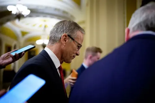 رجل يرتدي بدلة رسمية، يبدو أنه يتحدث مع مجموعة من الأشخاص في ممر مجلس الشيوخ، مع التركيز على النقاشات حول ميزانية الحكومة.